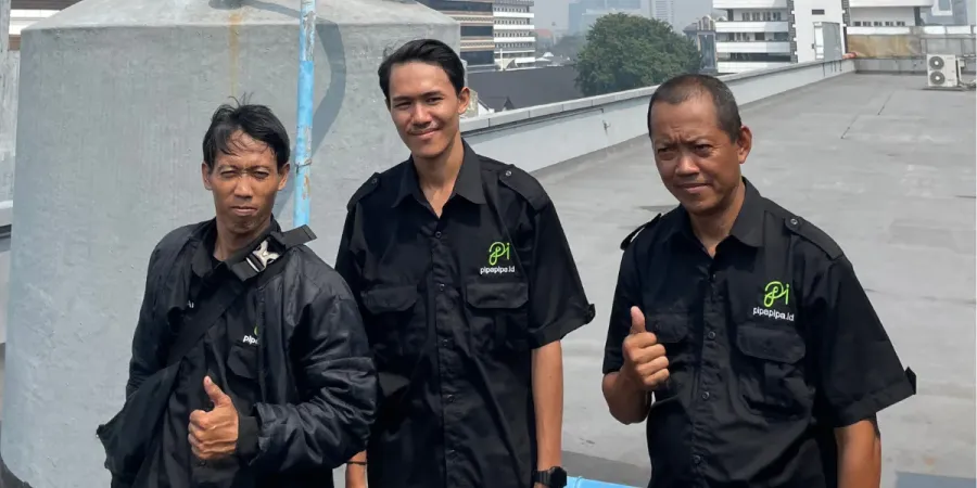 Tiga teknisi PipaPipa.id berseragam di atap gedung, berdiri di samping toren air yang baru dicuci