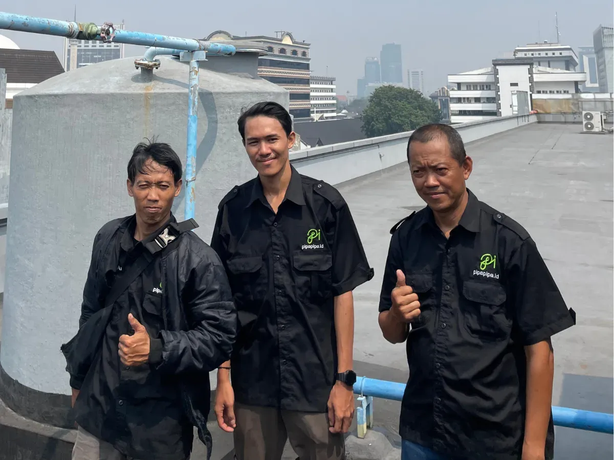 Tiga teknisi PipaPipa.id berseragam di atap gedung, di samping toren dan jalur pipa air